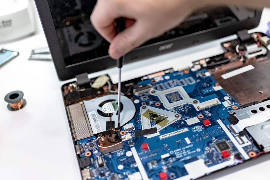 Hand repairing a laptop motherboard with a screwdriver, highlighting tech maintenance.